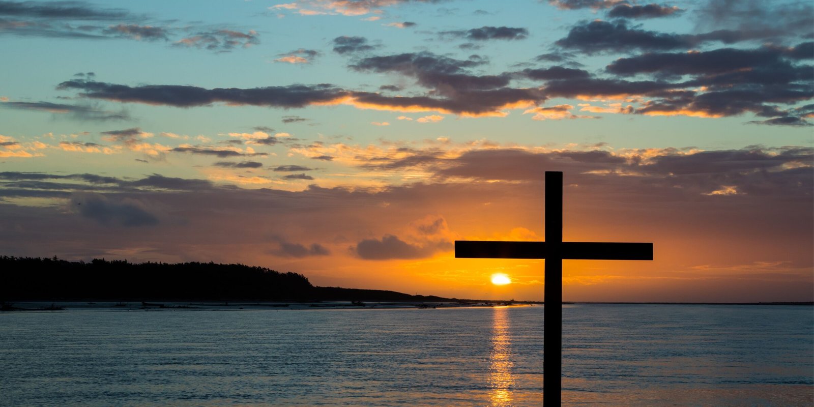 A wooden cross silhouetted against a golden sunrise over distant mountains